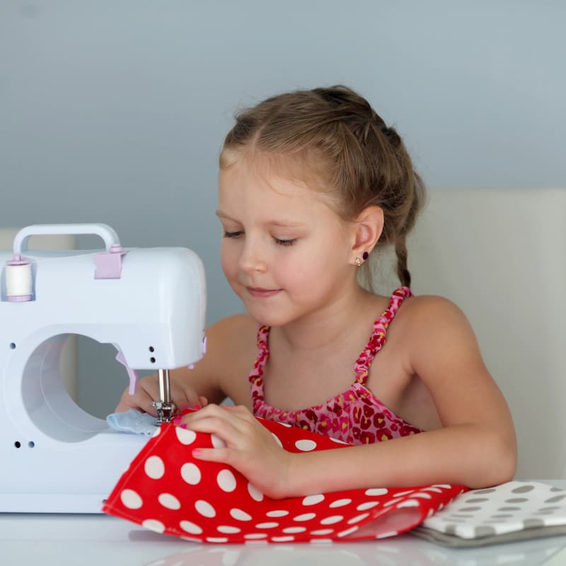 Young girl using a sewing machine to stitch red fabric with white polka dots.