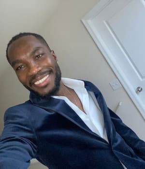 Text: Adrian smiling in a navy blazer and white shirt, standing indoors