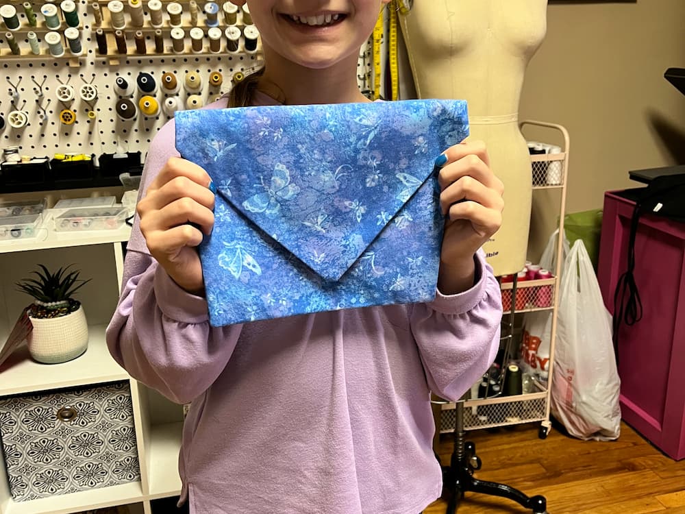 Smiling child proudly holding a handmade blue fabric envelope clutch with a butterfly print.