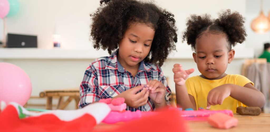 Two young girls focused on creating shapes with colorful modeling clay at a table.